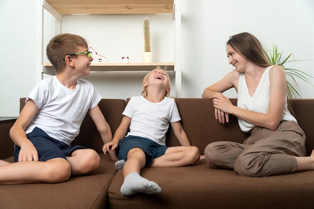 Une jeune maman et deux enfants sont assis sur un canapé et s'amusent à parler. Relations familiales amicales.