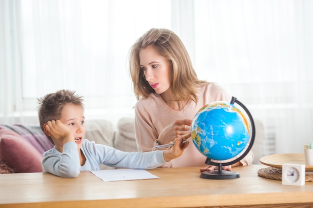 Jeune maman enseigne son petit fils à la maison. Maman et son enfant étudient la géographie à l'intérieur