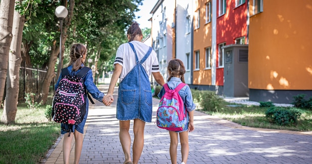 Jeune maman est accompagnée de petites filles à l'école, vue arrière.