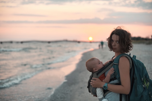 Une jeune maman est sur la plage avec son bébé en écharpe