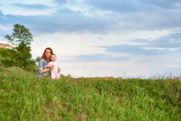 Jeune maman étreignant jolie petite fille assise sur l&#39;herbe dans le champ.