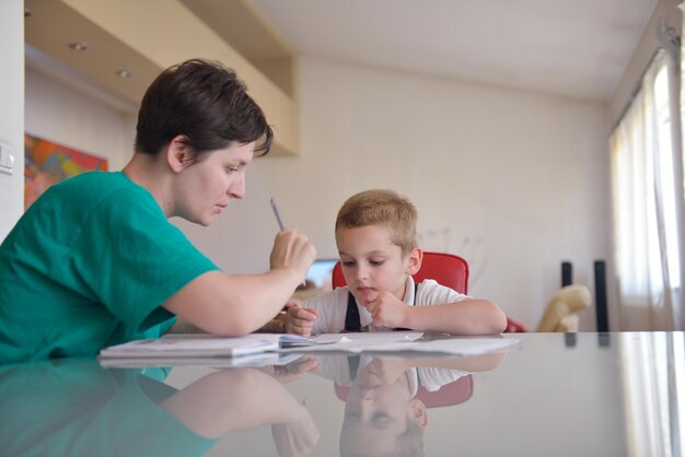 jeune maman femme faisant du travail à domicile avec un garçon de l'école élémentaire à la maison dans la cuisine