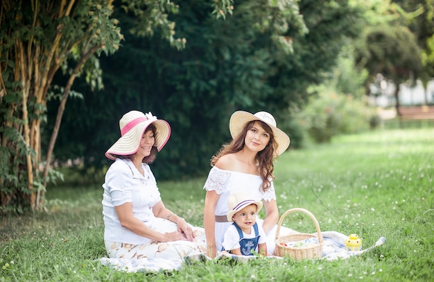 Une jeune maman, une grand-mère et un petit fils jouent dans une clairière. Pique-nique. Printemps. L'été. Chaleur. La famille est assise sur l'herbe.