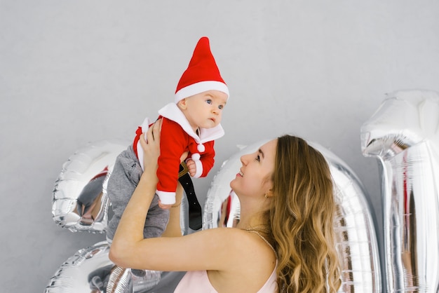 Une jeune maman heureuse tient un bébé dans un costume de Père Noël dans ses bras, contre le nombre de 20. Noël et nouvel an 2020