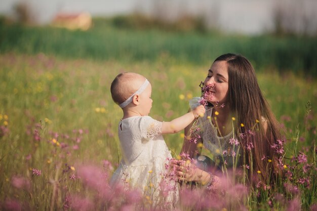 Jeune maman et jolie petite fille marchent et jouent dans le champ avec des fleurs sauvages.