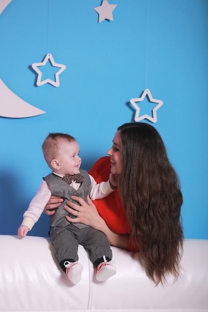 Jeune maman avec mignon petit garçon sur un canapé blanc. mur bleu avec une lune blanche et des étoiles sur un mur.