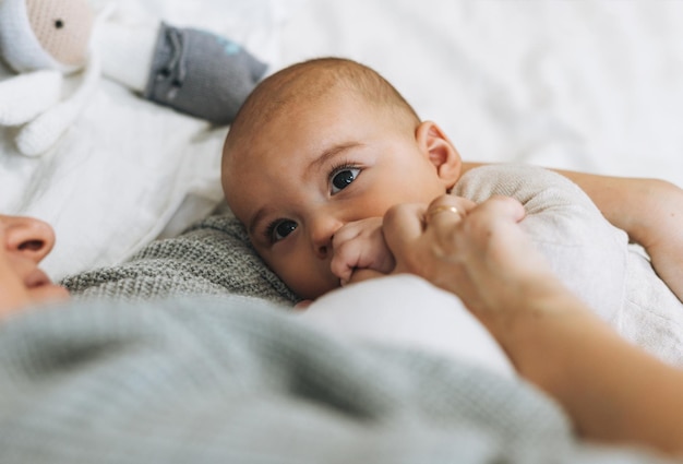 Jeune maman avec mignon petit garçon mère sein nourrit bébé sur le lit tons naturels