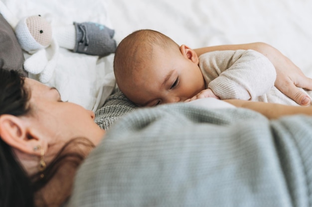 Jeune maman avec mignon petit garçon mère sein nourrit bébé sur le lit tons naturels