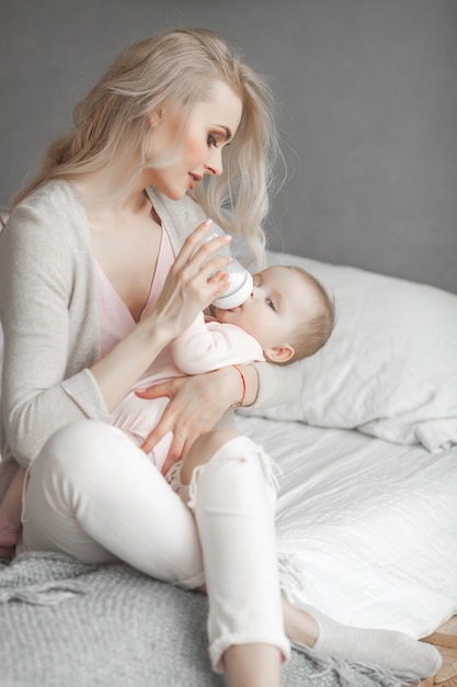 Jeune maman nourrit sa petite fille mignonne avec une bouteille de lait maternisé. Femme avec son nouveau-né à la maison. Maman s'occupe d'un enfant. Alternative à l'allaitement maternel.