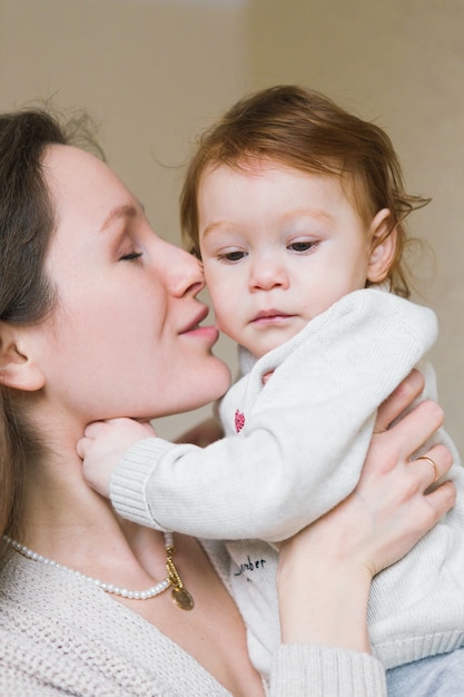 Jeune maman avec petits enfants sur les mains, assis sur le canapé. Jeune femme, baisers, fille