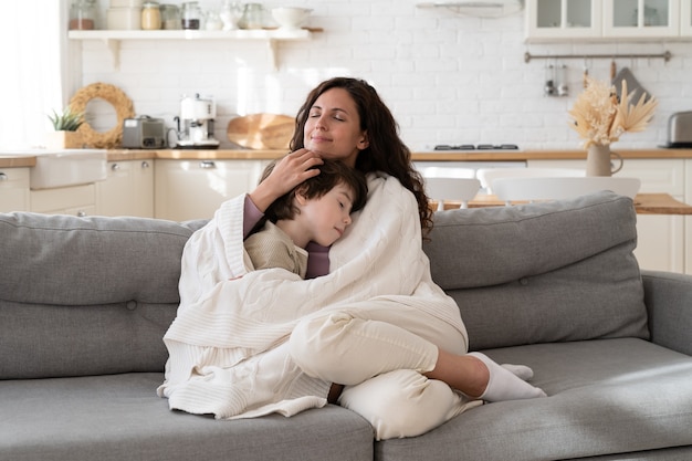 Jeune maman s'asseoir sur un canapé confortable se détendre avec son fils d'âge préscolaire recouvert d'une couverture le matin du week-end à la maison