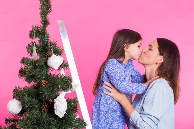 Jeune maman et sa fille avec arbre de Noël sur fond rose