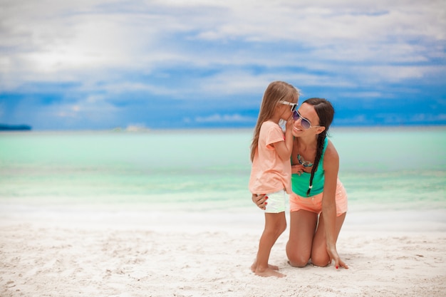 Jeune maman et sa mignonne petite fille chuchotant sur la plage blanche