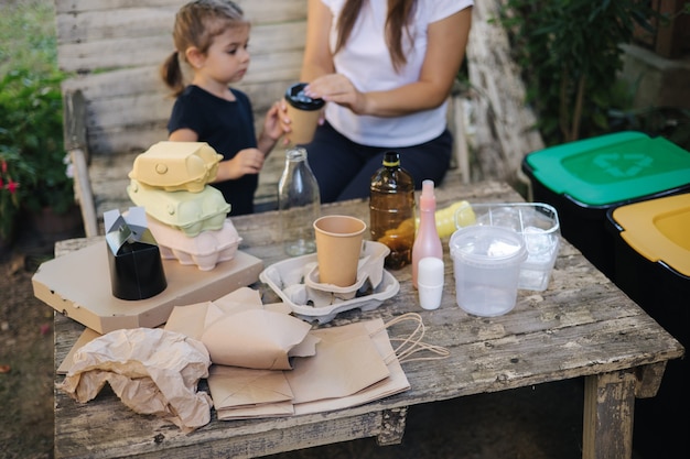 Jeune maman avec sa petite fille se préparant à recycler différents types de déchets et à mettre