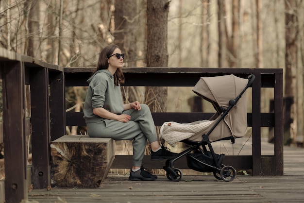 La jeune maman se détend sur le banc en bois pendant que son bébé dort dans la poussette La mère avec son enfant dans le parc pour prendre l'air