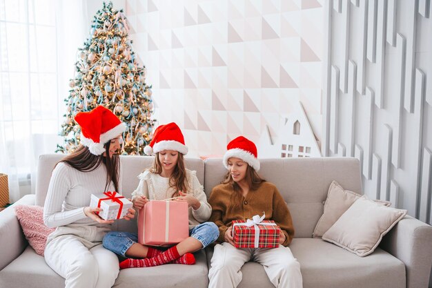 Jeune maman et ses petites filles avec des cadeaux sous le sapin de Noël