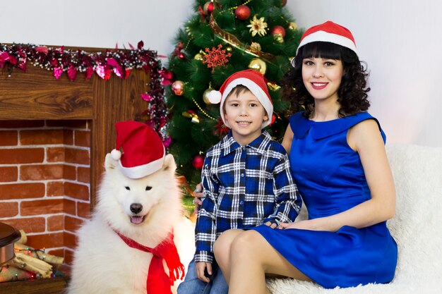 Une jeune maman avec son fils et un chien devant un sapin de Noël.