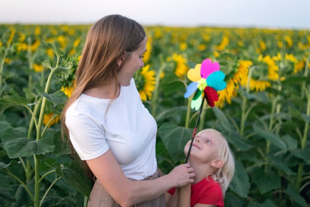 Jeune maman et son fils marchent dans un champ de tournesol avec un jouet de moulin à vent. Concept d'énergie verte. Famille heureuse.