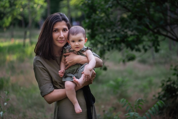 Jeune maman tient bébé dans les bras dans les rayons du coucher du soleil dans le parc.