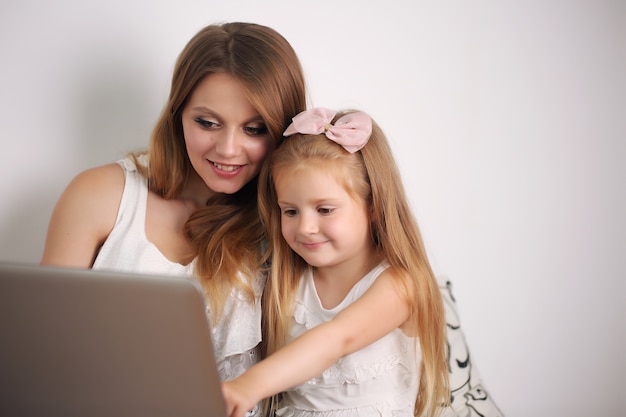 La jeune maman travaille avec sa fille sur le PC à la maison.