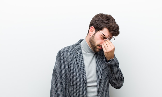 Jeune manager homme stressé, malheureux et frustré, touchant le front et souffrant de migraine de maux de tête sévères contre le blanc