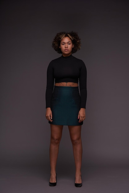 Jeune mannequin femme sérieuse en vêtements décontractés intelligents posant devant un mur gris