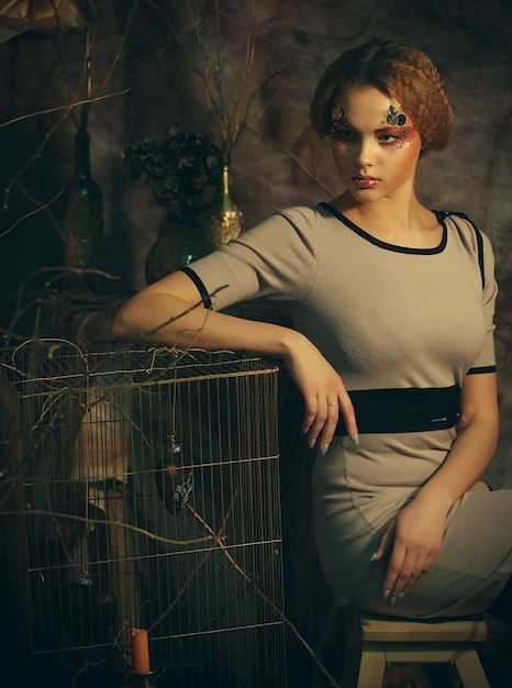 Jeune mannequin avec maquillage créatif assis sur un tabouret