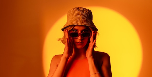 Un jeune mannequin à la mode portant des lunettes de soleil à la mode et un chapeau élégant sur un fond orange posant