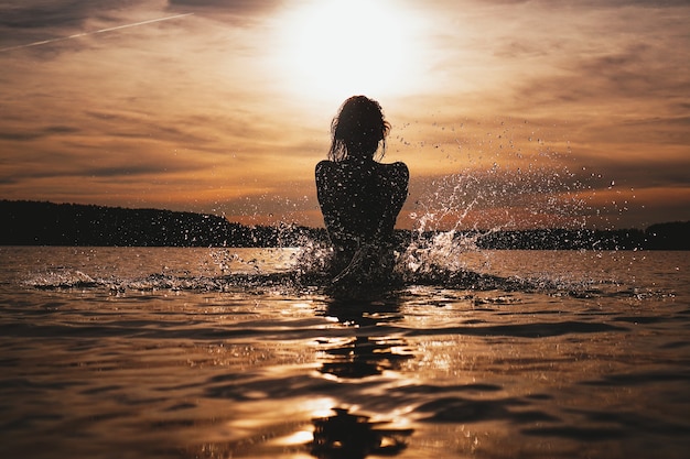 Jeune mannequin nageant dans l'heure du coucher du soleil sur la mer