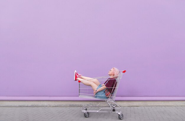 Jeune mannequin pose avec un chariot sur l'arrière-plan d'un mur violet