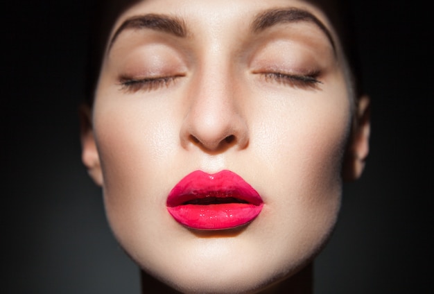 Jeune mannequin avec les yeux fermés et les lèvres roses sur fond noir. Isoler