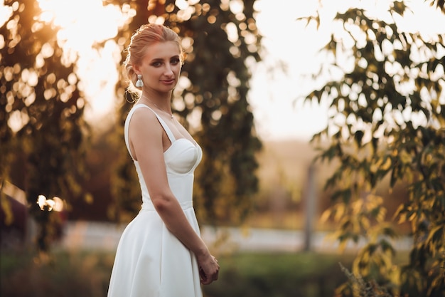 Jeune mariée caucasienne en robe blanche avec une belle coupe de cheveux se promène dans le jardin d'été seul