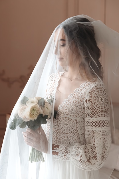 Jeune mariée dans une belle robe en dentelle bohème sous un long voile.