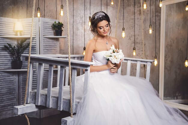 Jeune mariée heureuse portant une belle robe luxuriante dans la chambre avec beaucoup d'ampoules