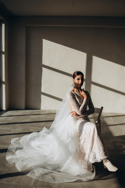 Jeune mariée en robe de mariée blanche tenant un bouquet et regardant loin à la maison