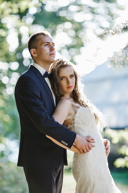 jeune mariée tient la main du marié sur sa taille alors qu&#39;ils posent dans un parc verdoyant dans une journée ensoleillée