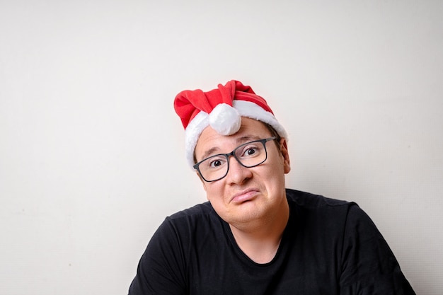 Jeune mec drôle avec un chapeau de Noël sur mur blanc. Père Noël triste. Noël