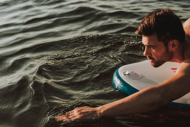 Jeune mec est allongé sur les vagues et nage.