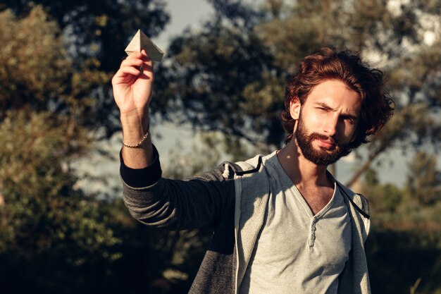 Jeune mec heureux jouant en plein air avec un avion en papier.