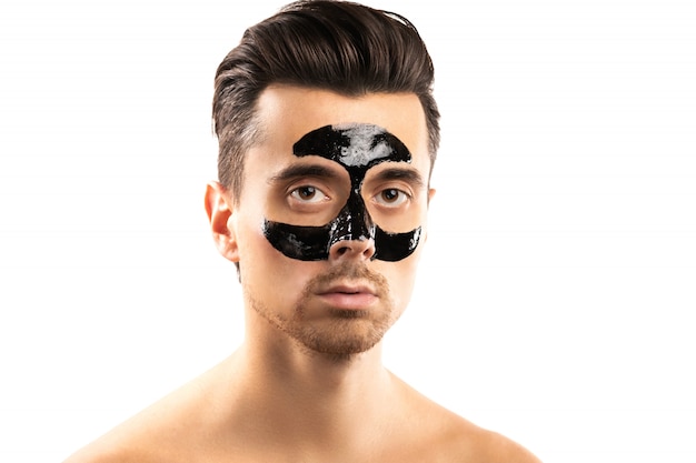 Jeune mec avec un masque de charbon de bois noir sur son visage sur blanc.
