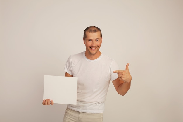 un jeune mec mignon dans un t-shirt blanc tient une feuille de papier blanche dans ses mains