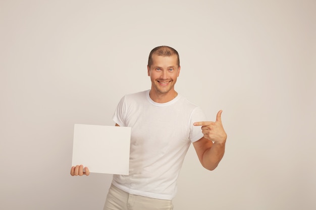 un jeune mec mignon dans un t-shirt blanc tient une feuille de papier blanche dans ses mains