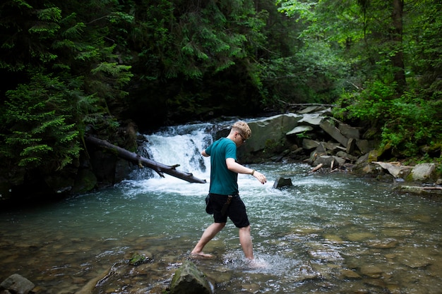 Jeune mec se tient au bord de la rivière dans le contexte d'une cascade