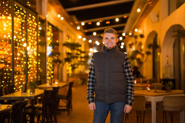 Jeune mec souriant posant la nuit au café