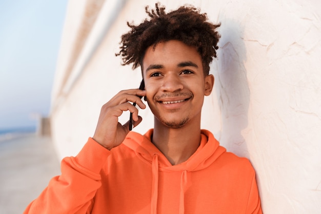 Jeune mec sportif à l'extérieur sur la plage, parler par téléphone mobile