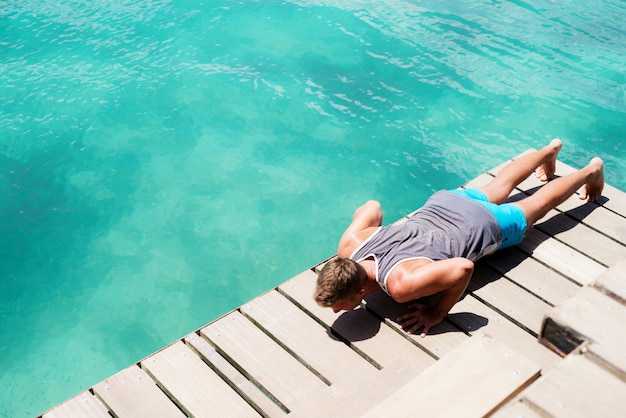 Jeune mec sportif faisant des pompes au bord de la mer.