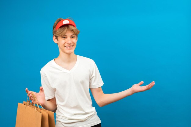 Jeune mec en t-shirt blanc décontracté avec sac en papier isolé sur fond bleu portrait en studio Concept de mode de vie des gens Maquette copie espace Tenir le sac d'emballage avec les achats