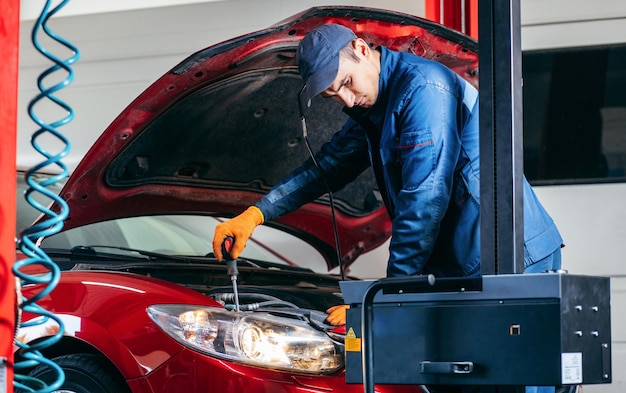 Jeune mécanicien ajustant les phares de la voiture moderne rouge en service automatique