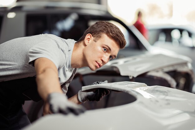 Un jeune mécanicien contrôle une voiture blanche dans un garage.