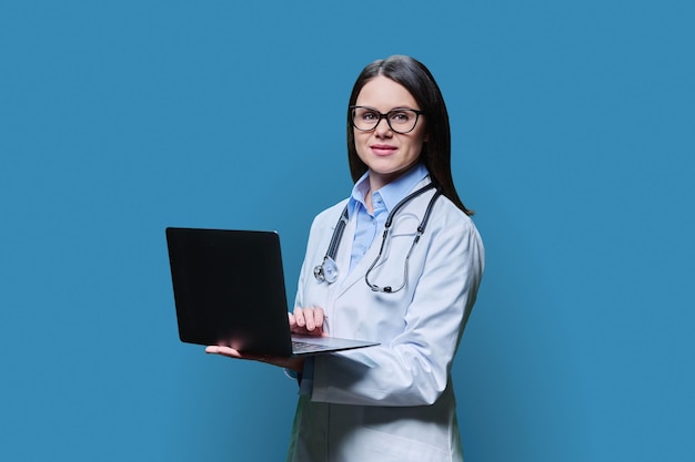 Une jeune médecin amie utilisant un ordinateur portable sur fond bleu